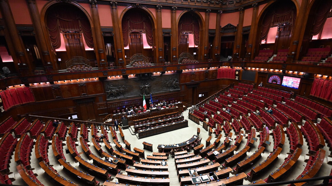 L'immagine rappresenta l'Aula della Camera, un ampio spazio interno con file di sedili e tavoli in legno. Si svolgono dichiarazioni di voto al decreto fiscale. L'ambiente &egrave; caratterizzato da un'architettura tipica di un edificio parlamentare, simile a un auditorium o a un teatro. Sono presenti persone che partecipano all'evento.