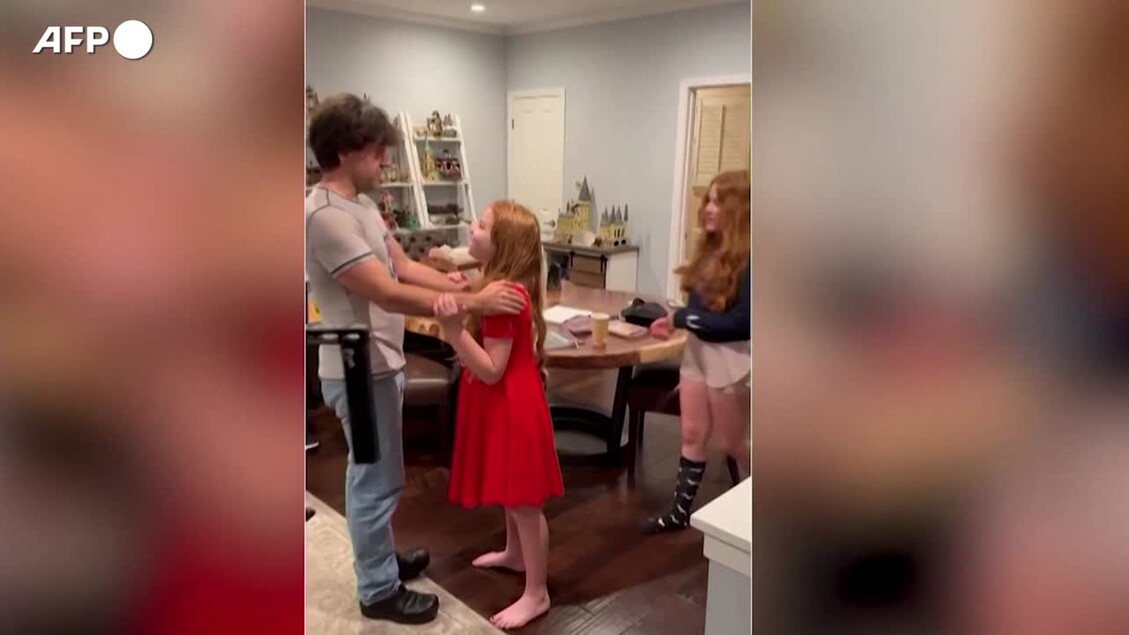 L'immagine mostra l'annuncio del vincitore del Premio Nobel per la medicina, Deisseroth, alla sua famiglia. Sono presenti un uomo e una ragazza che ballano. L'ambiente &egrave; interno, probabilmente in un contesto festivo. Altri dettagli includono persone, abbigliamento e un muro.