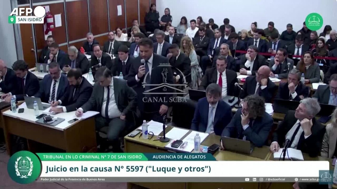 L'immagine mostra un'udienza legale, con un gruppo di persone sedute a scrivanie. Un uomo in abito formale tiene un microfono. Si svolge l'arringa finale del pubblico ministero al processo Maradona, con la dichiarazione: Diego abbandonato alla sua sorte. L'ambiente &egrave; interno, probabilmente in un tribunale, e vi sono elementi come tavoli e computer.