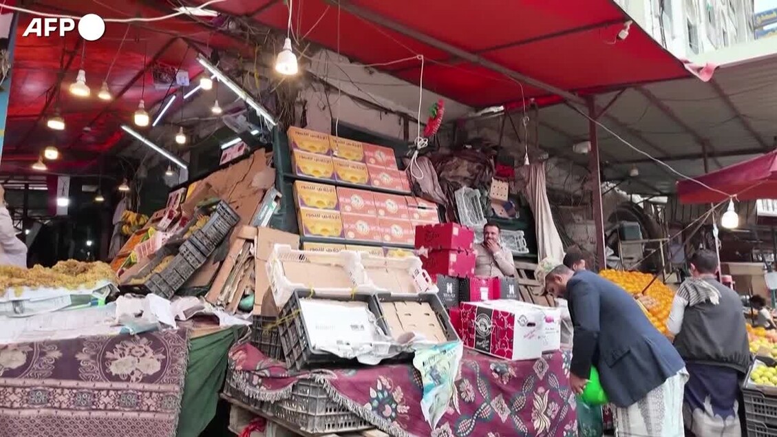 In Yemen, il blocco imposto dagli Houthi aggrava la carenza di generi alimentari. Si osserva un gruppo di persone in un mercato, dove si svolge un'attivit&agrave; di commercio. Sono presenti scatole e ceste, tipiche di un bazar. L'ambiente &egrave; caratterizzato da un soffitto rosso.