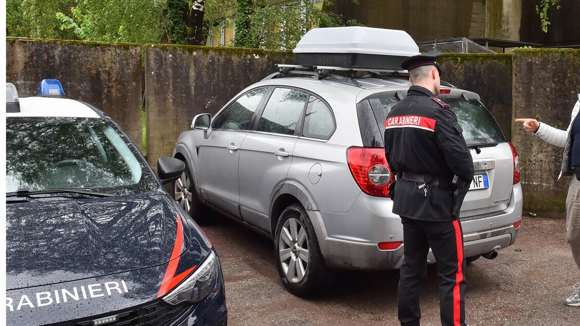L'immagine mostra l'auto di Sonia Bottecchiari, un veicolo di tipo FIAT. Un uomo in uniforme si trova accanto all'auto. Sullo sfondo, ci sono il pap&agrave; e i nonni della famiglia piacentina scomparsa, presenti al campo base. L'ambientazione &egrave; all'aperto, suggerendo un contesto di trasporto o di incontro familiare.