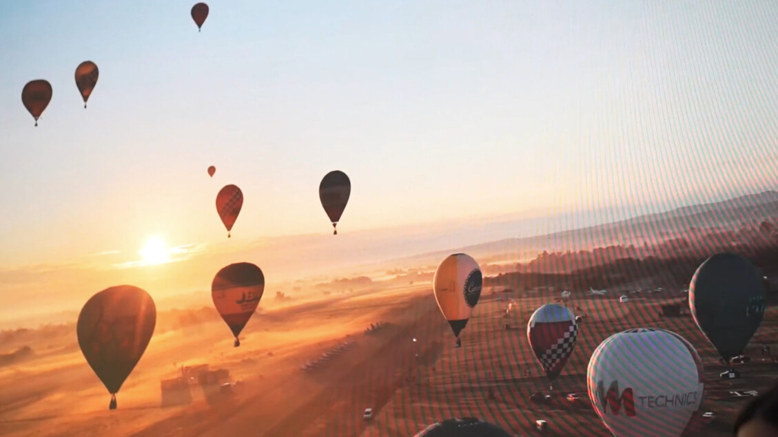 L'immagine presenta la Balloon Cup - Dalla mongolfiera alla stratosfera, un evento che coinvolge mongolfiere nel cielo. Sono visibili mongolfiere che volano sopra un paesaggio desertico, creando un'atmosfera di natura e avventura all'aperto. Il cielo &egrave; un elemento centrale della scena, arricchita dalla presenza di veicoli aerei.