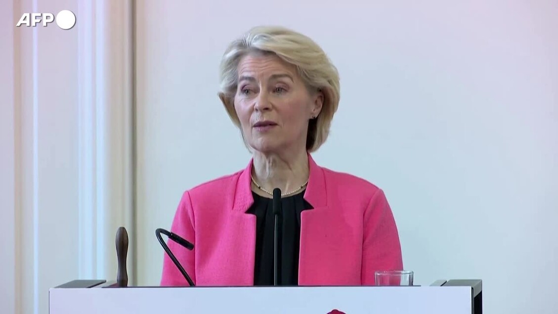 Ursula von der Leyen &egrave; riconoscibile nell'immagine. Indossa una giacca rosa e si trova in un contesto in cui si discute di misure contro la dipendenza dai social media. Sono presenti altre persone, suggerendo un ambiente di pubblico. L'immagine rappresenta un momento di discorso pubblico.