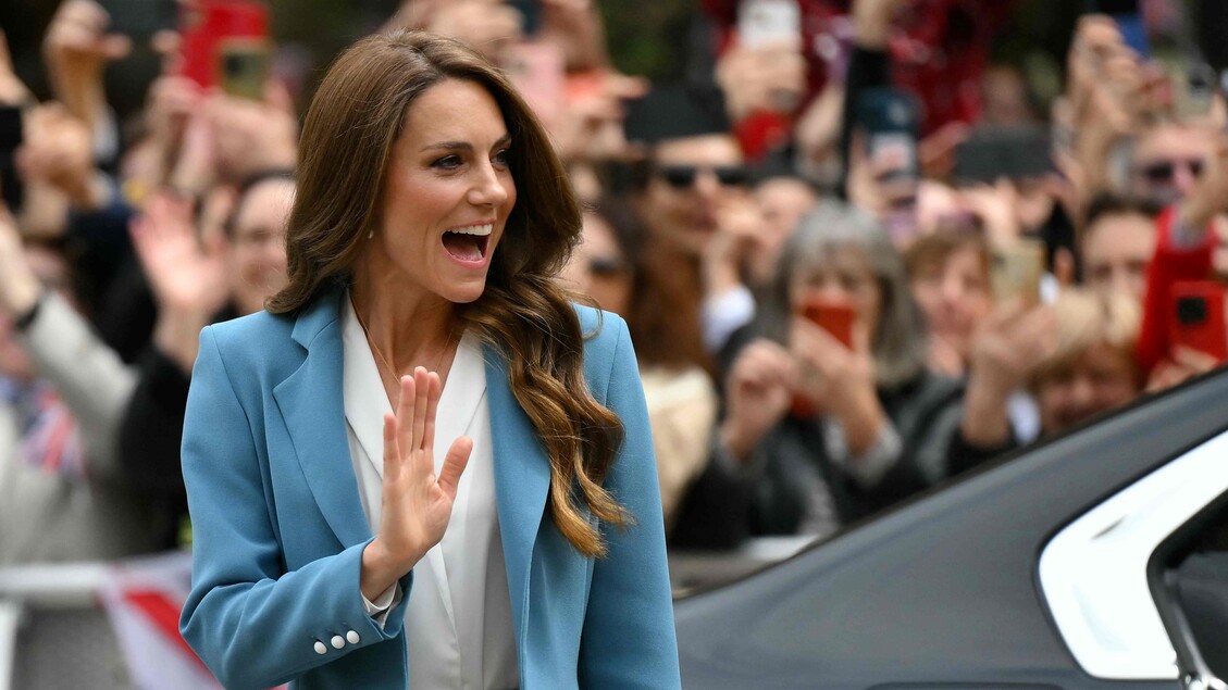 La Principessa Kate arriva in piazza a Reggio Emilia. &Egrave; una donna in un abito blu che saluta con la mano. La scena si svolge all'aperto e la figura &egrave; visibile con dettagli come il viso e l'abbigliamento.