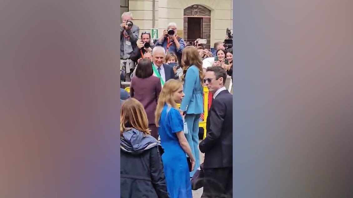 La principessa Kate riceve il Primo Tricolore a Reggio Emilia. Un gruppo di persone si trova in una folla. Tra di loro, &egrave; presente una donna in un vestito blu. La scena include adulti e uomini, tutti vestiti in abiti vari.