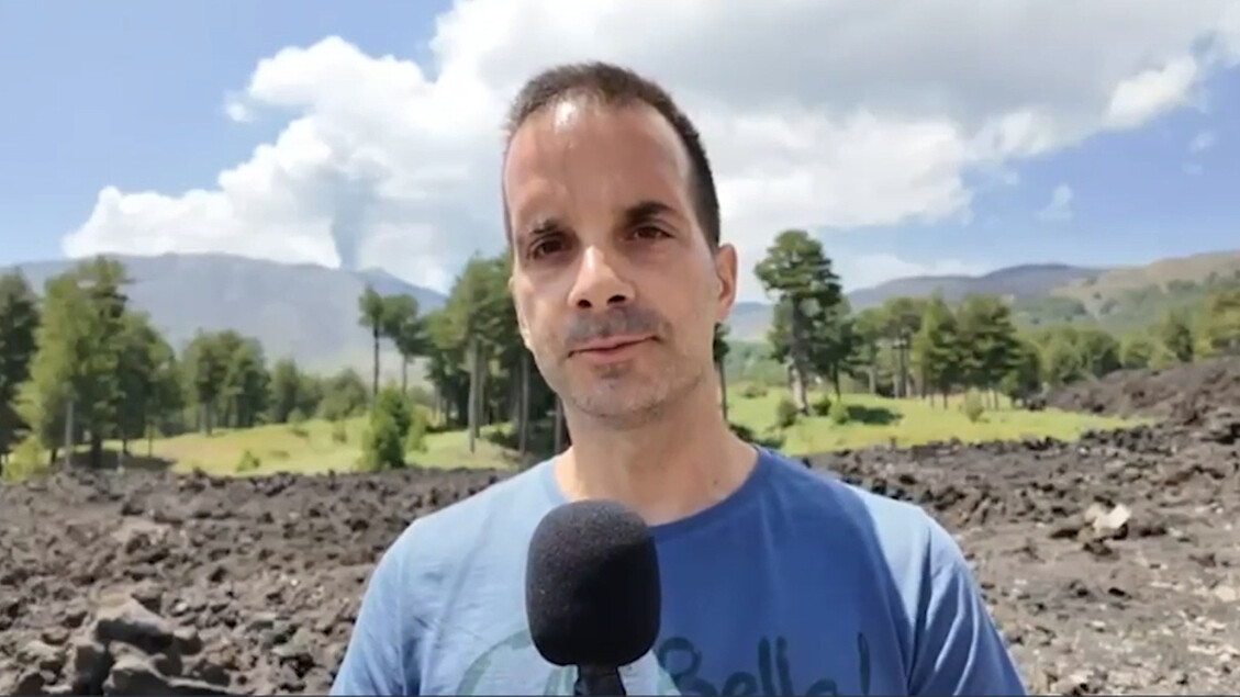 Il test dell'Agenzia spaziale italiana si svolge sull'Etna, un luogo ideale per osservare la Luna. Un uomo si trova di fronte a un microfono, mentre il suo volto &egrave; visibile in primo piano. L'immagine rappresenta un contesto all'aperto, con il cielo e le nuvole sullo sfondo.