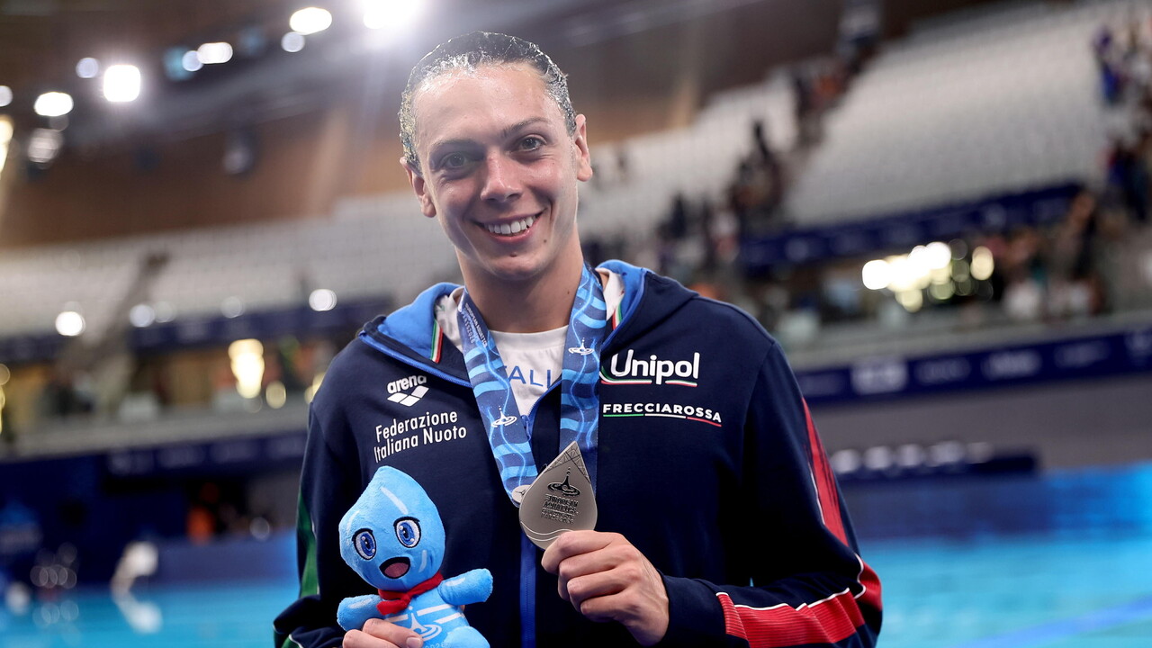 Un uomo partecipa ai Campionati Europei di Nuoto a Parigi nel 2026. Tiene in mano una medaglia e un piccolo animale di peluche blu. Indossa un abbigliamento sportivo, visibile insieme al suo volto.