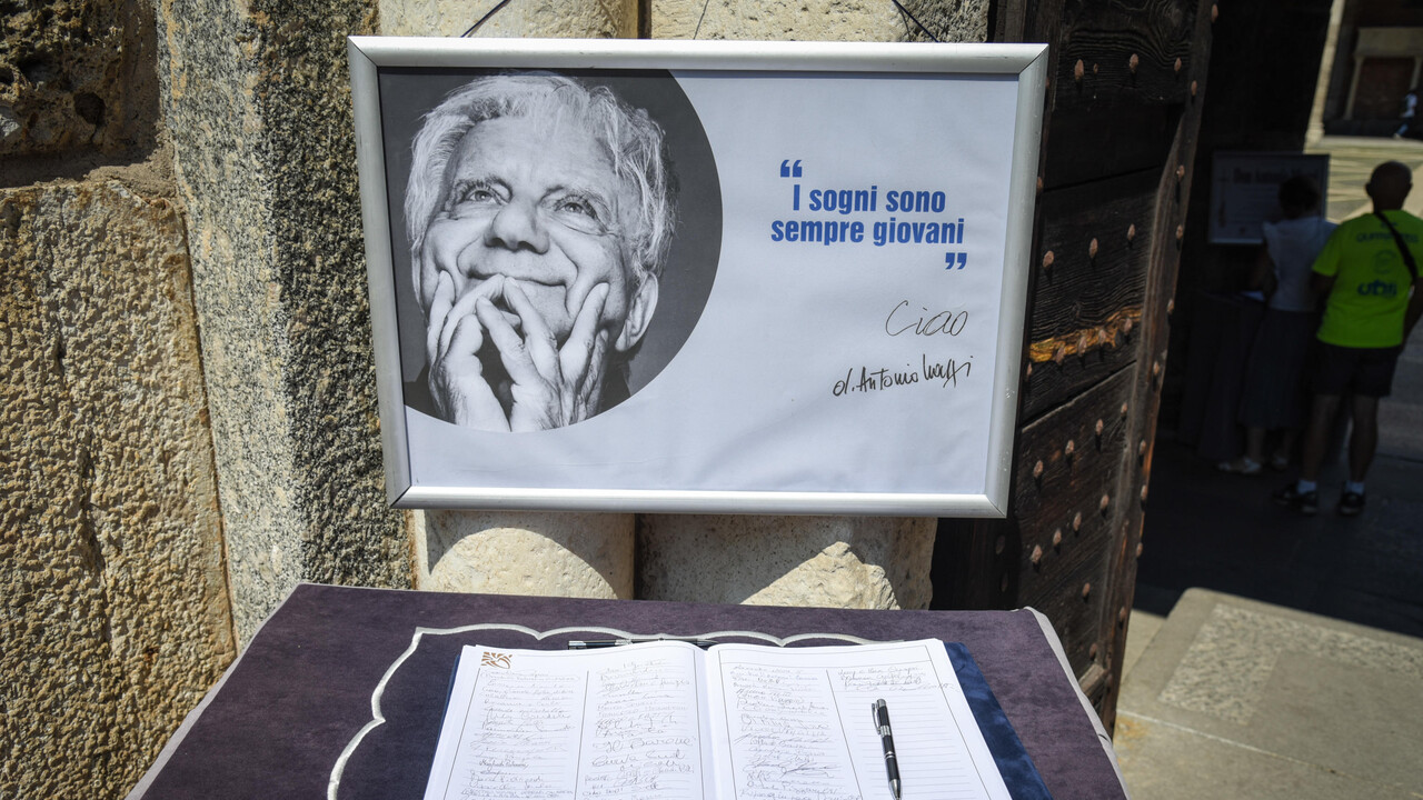 Si svolge il funerale di Don Mazzi nella Basilica di S. Ambrogio a Milano. Sono presenti un segno, una penna e un libro su un tavolo. Un testo significativo recita sempre giovani e I sogni sono. La scena include anche una persona.