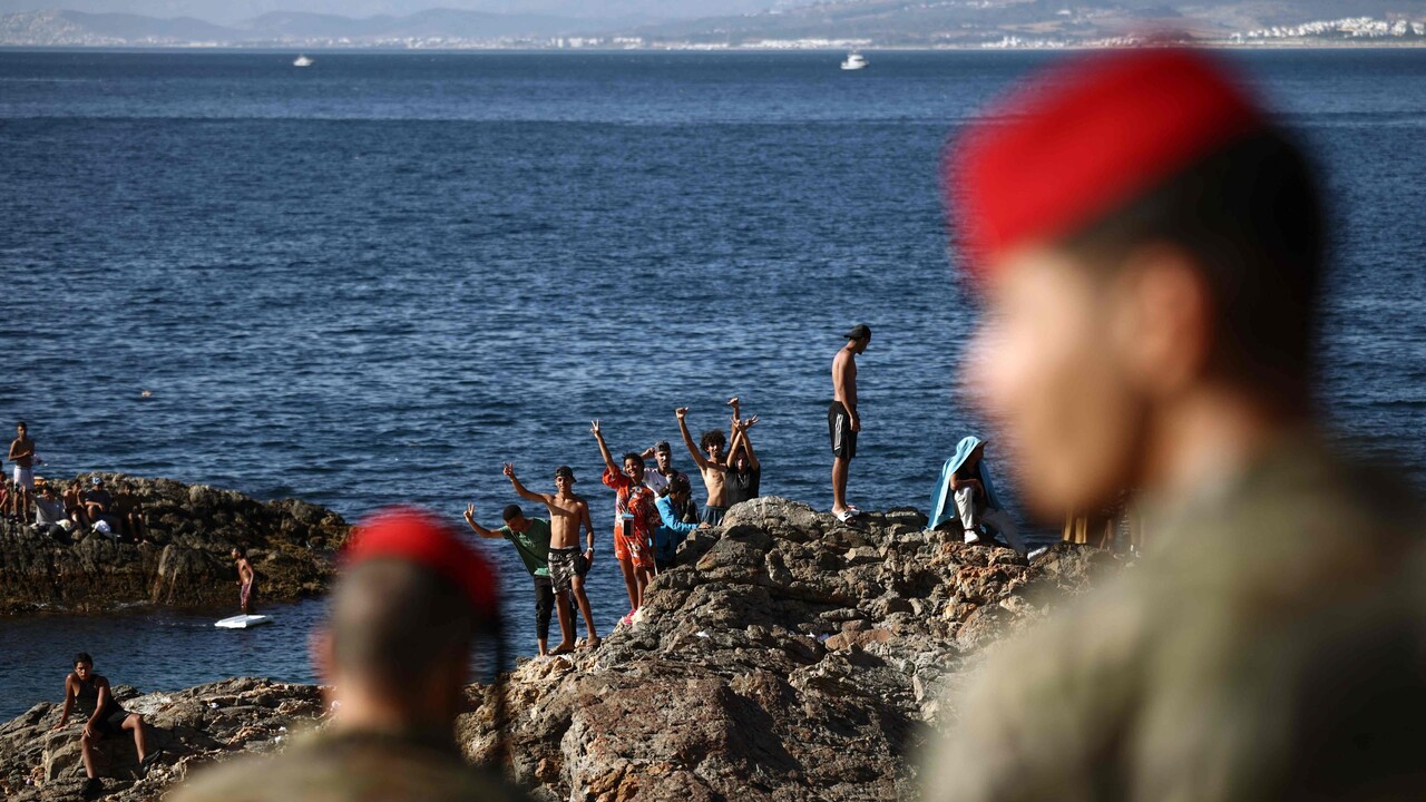 Un gruppo di militari spagnoli &egrave; presente con un gruppo di migranti a Ceuta, il 2 agosto 2026. Si osservano persone su una spiaggia rocciosa, vicino all'acqua. L'ambiente &egrave; naturale, con rocce e mare visibili. La scena si svolge all'aperto, con adulti e uomini tra i presenti.