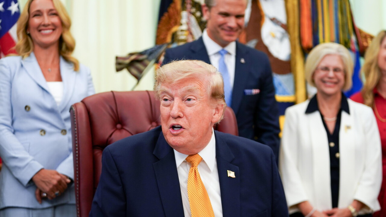 Donald Trump &egrave; riconoscibile nell'immagine. Annuncia un ordine esecutivo che stabilisce la Commissione per i Coniugi Militari Presidenziali. &Egrave; un uomo in abito formale, con giacca e cravatta. L'immagine presenta anche altre persone, suggerendo un contesto ufficiale e formale.