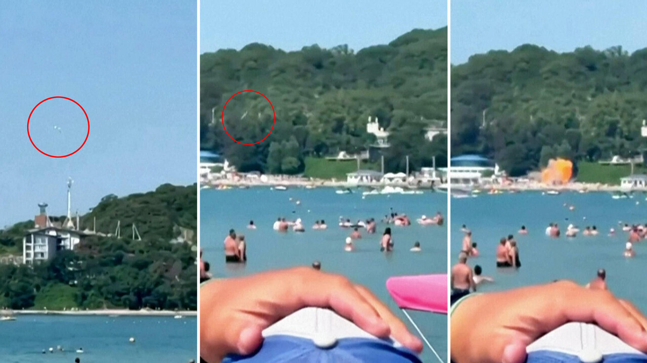 Un drone ucraino si trova sulla spiaggia, vicino al cosiddetto 'Palazzo di Putin'. La scena mostra una spiaggia affollata di persone in acqua, con un edificio bianco visibile in lontananza. L'ambiente &egrave; caratterizzato da attivit&agrave; ricreative all'aperto, come sport acquatici e nuoto, in un contesto estivo. La presenza di un frisbee suggerisce ulteriori attivit&agrave; di svago.