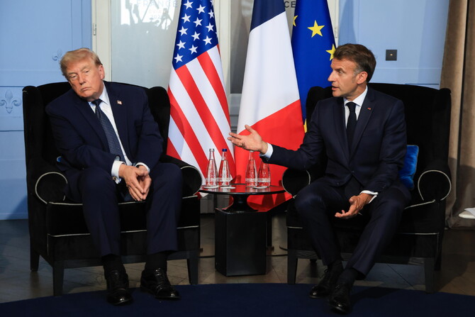 Il presidente degli Stati Uniti, Donald Trump, e il presidente francese, Emmanuel Macron, sono riconoscibili nell'immagine. Entrambi sono seduti su sedie e indossano abiti formali, mentre discutono. Sullo sfondo &egrave; visibile una bandiera degli Stati Uniti. L'evento si svolge durante il vertice del G7 a Evian-les-Bains, in Francia. Una folla di persone &egrave; presente, contribuendo all'atmosfera ufficiale dell'incontro.
