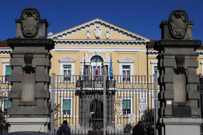 L'immagine mostra un edificio giallo con un ingresso recintato. Questo edificio &egrave; associato all'Istituto Spallanzani, che ha costituito una task force per affrontare una nuova variante del Covid. Il contesto suggerisce un ambiente urbano, con un cielo blu visibile sopra l'edificio.