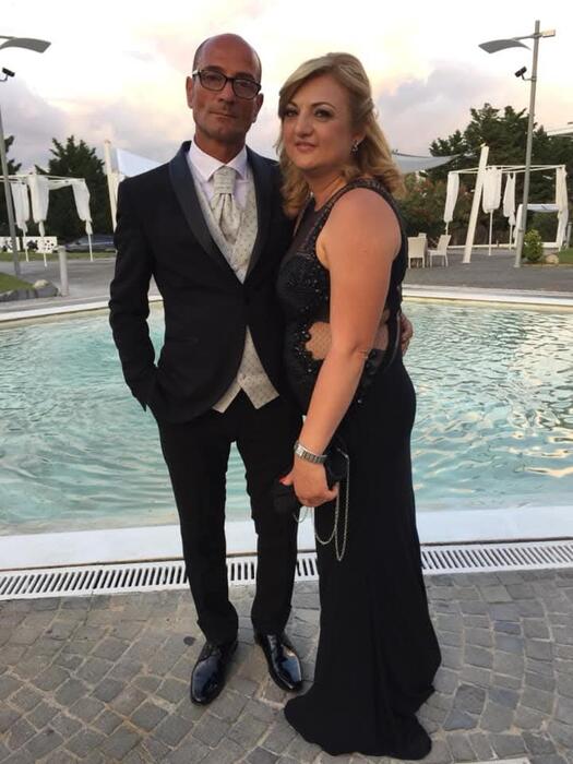 Un uomo e una donna indossano abiti formali. L'immagine &egrave; associata a un contesto di giustizia, poich&eacute; la moglie dell'operaio morto esprime il desiderio di ottenere giustizia. Gli abiti includono un completo e un vestito elegante.