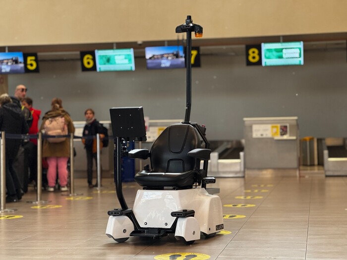 Un robot per l'assistenza ai disabili &egrave; presente in un aeroporto a Treviso. Il robot &egrave; un veicolo in bianco e nero. All'interno dell'aeroporto, ci sono anche sedie e un monitor. La scena &egrave; caratterizzata da un ambiente interno, con pavimento pulito e arredamento. Una persona &egrave; visibile nell'immagine.