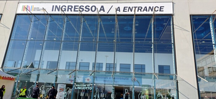 L'immagine mostra un grande edificio di vetro, che funge da centro congressi, situato al Salone del Libro di Torino. L'evento presenta l'Uici con Braille e audiolibri. &Egrave; visibile un'insegna che indica l'ingresso. L'architettura dell'edificio &egrave; moderna e si possono notare elementi come pannelli solari.