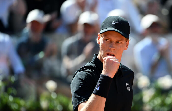 L'immagine rappresenta il torneo di tennis Italian Open. &Egrave; visibile un uomo che indossa una maglietta nera e un cappello. Ci sono altre persone presenti, suggerendo un evento sportivo all'aperto. L'atmosfera &egrave; quella di una competizione atletica.