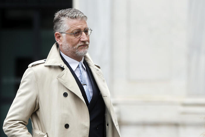 Un uomo indossa un trench coat. Il contesto riguarda il ministero della cultura, scosso dal licenziamento di Giuli e dalla reazione di Arianna Meloni, che afferma che si sta creando un caso su nulla.