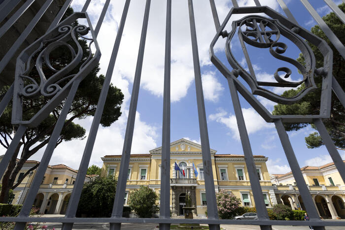 L'immagine mostra l'ingresso dello Spallanzani a Roma, un edificio che presenta un'architettura distintiva. Sono visibili elementi come un cancello e una statua. Il contesto &egrave; all'aperto, con un cielo nuvoloso e alberi nelle vicinanze. Recentemente, sono stati analizzati campioni biologici di un 25enne calabrese per il virus Hantavirus.