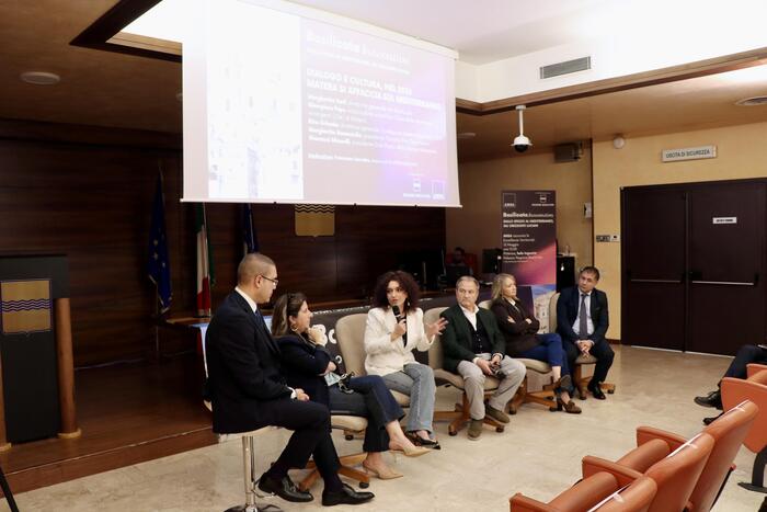 A Potenza si svolge la seconda tappa del tour "Italia Innovativa". Nella sala, un gruppo di persone &egrave; seduto su sedie. Una donna parla a questo gruppo, mentre un uomo si trova davanti a uno schermo. L'ambiente &egrave; un seminario con un pubblico adulto, composto da uomini e donne.