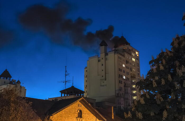 A Kiev, i droni russi riprendono gli attacchi mentre termina un cessate il fuoco di tre giorni. Si osserva un edificio con fumi neri che fuoriescono, segno di un attacco in corso. Il cielo &egrave; coperto di fumi e nuvole, contribuendo a un'atmosfera di conflitto. La scena &egrave; caratterizzata dalla presenza di una torre e da un contesto di guerra all'aperto.