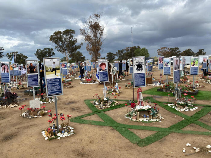 Israele istituisce il tribunale speciale militare per i crimini del 7 ottobre. La scena mostra una veduta del sito del Nova Festival, con un gruppo di segnali in un campo. Sono presenti anche alberi e una torre radio sullo sfondo. L'ambiente &egrave; all'aperto, in un contesto urbano, con un cielo nuvoloso.