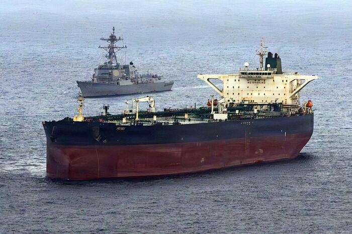 L'immagine mostra una grande nave in acqua, identificata come una nave mercantile. Il contesto &egrave; legato a tensioni geopolitiche tra Stati Uniti, Iran e Israele, suggerendo un ambiente di conflitto. La scena &egrave; all'aperto e rappresenta un elemento di trasporto marittimo.