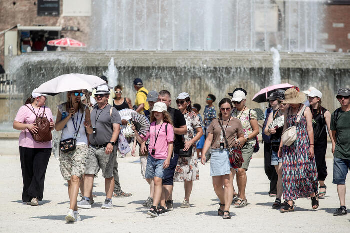 Un gruppo di persone cammina davanti a una fontana. La scena si svolge all'aperto, in un contesto urbano. Si osservano adulti, uomini e donne, alcuni indossano abbigliamento estivo. Domenica, 23 citt&agrave; avranno il bollino rosso per il caldo.
