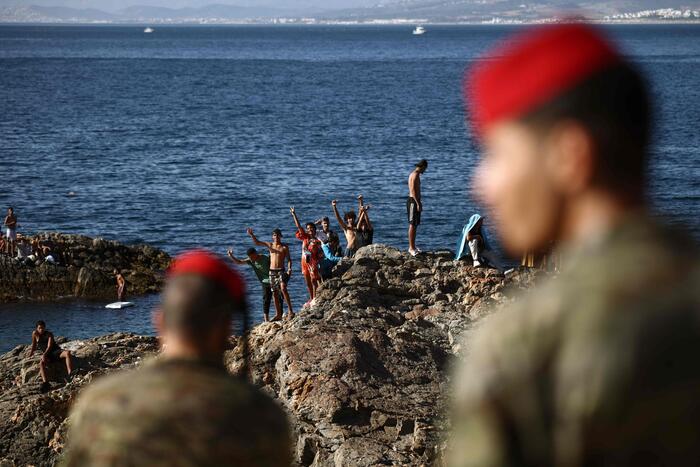 Un gruppo di militari spagnoli &egrave; presente con un gruppo di migranti a Ceuta, il 2 agosto 2026. Si osservano persone su una spiaggia rocciosa, vicino all'acqua. L'ambiente &egrave; naturale, con rocce e mare visibili. La scena si svolge all'aperto, con adulti e uomini tra i presenti.