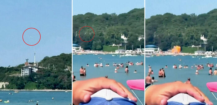 Un drone ucraino si trova sulla spiaggia, vicino al cosiddetto 'Palazzo di Putin'. La scena mostra una spiaggia affollata di persone in acqua, con un edificio bianco visibile in lontananza. L'ambiente &egrave; caratterizzato da attivit&agrave; ricreative all'aperto, come sport acquatici e nuoto, in un contesto estivo. La presenza di un frisbee suggerisce ulteriori attivit&agrave; di svago.