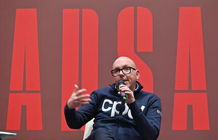 A Torino si svolge la presentazione di PHOTOANSA 2025. Un uomo &egrave; seduto su una sedia e tiene un microfono. Sono presenti altre persone e un pubblico.