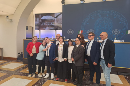 Un gruppo di ragazzi disabili, che include cuochi, meccanici e saldatori, partecipa a un progetto scuola-lavoro. Sono presenti insieme davanti a uno schermo e posano per una foto. Ludovico Einaudi &egrave; riconoscibile nell'immagine. Il contesto &egrave; indoor, con persone vestite in abiti formali.