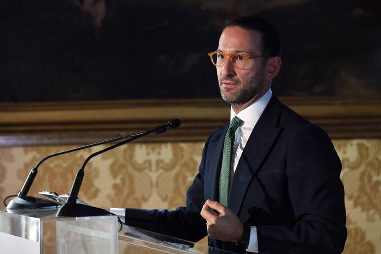 Un uomo in abito formale, con cravatta, si trova dietro a un podio. &Egrave; un oratore che sta parlando a un pubblico, composto da una folla di persone. Il contesto dell'immagine riguarda il rinvio della nomina del presidente della Consob.