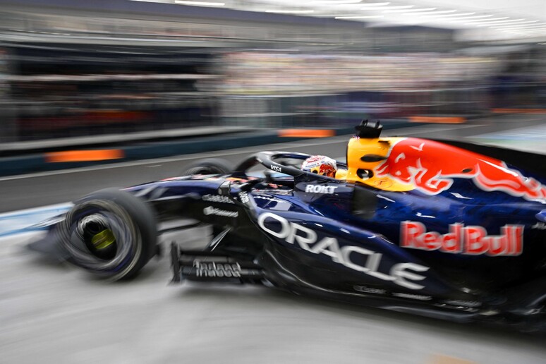 Max Verstappen &egrave; in pole position nella Sprint a Singapore, seguito da Charles Leclerc al terzo posto. La scena si svolge su un circuito di auto da corsa, caratterizzato da veicoli di Formula Uno. Sono presenti elementi tipici del motorsport, come pneumatici e ruote, che arricchiscono il contesto della gara.