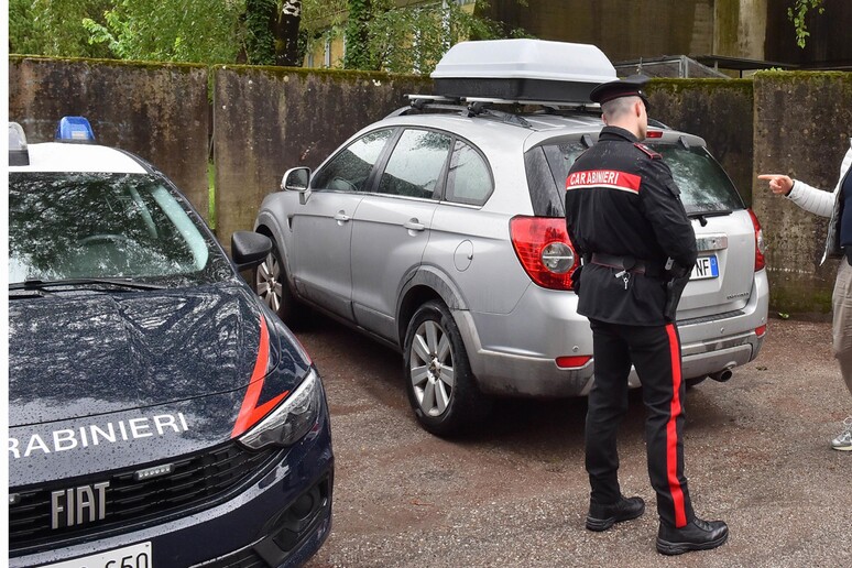 L'immagine mostra l'auto di Sonia Bottecchiari, un veicolo di tipo FIAT. Un uomo in uniforme si trova accanto all'auto. Sullo sfondo, ci sono il pap&agrave; e i nonni della famiglia piacentina scomparsa, presenti al campo base. L'ambientazione &egrave; all'aperto, suggerendo un contesto di trasporto o di incontro familiare.