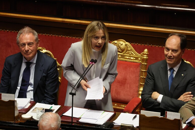 Giorgia Meloni &egrave; riconoscibile nell'immagine mentre parla a un podio con un microfono. Davanti a lei, un uomo in abito formale &egrave; seduto. L'ambiente &egrave; interno e suggerisce un contesto ufficiale, probabilmente legato a questioni di governo e gestione. Ci sono anche documenti su un tavolo, che possono indicare un incontro di lavoro o una conferenza.