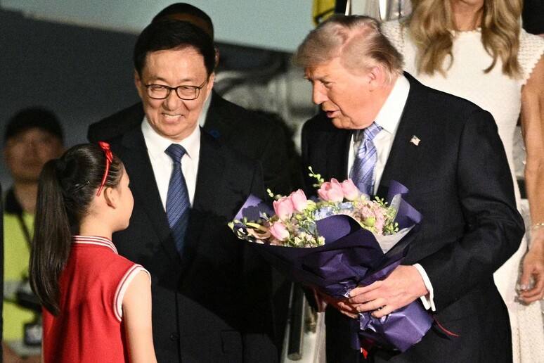 Un uomo in abito formale tiene un bouquet di fiori. &Egrave; presente anche una ragazza in un vestito rosso. Han Zheng e Donald Trump sono riconoscibili nell'immagine. L'ambientazione suggerisce un contesto di cerimonia.