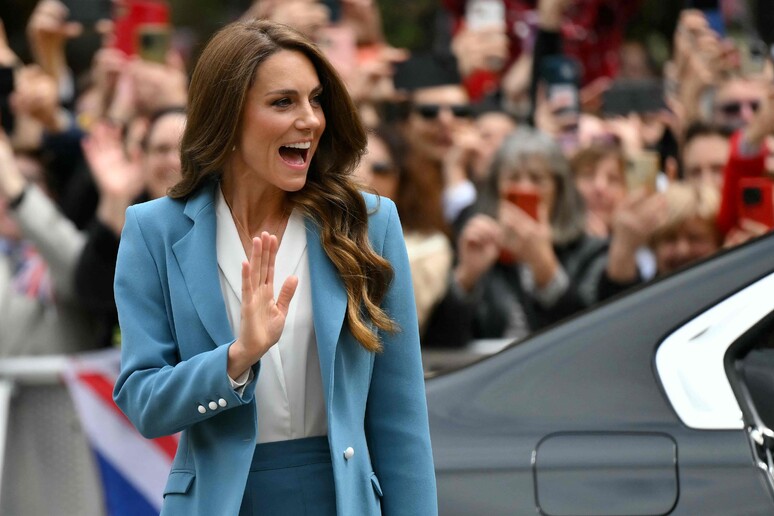 La Principessa Kate arriva in piazza a Reggio Emilia. &Egrave; una donna in un abito blu che saluta con la mano. La scena si svolge all'aperto e la figura &egrave; visibile con dettagli come il viso e l'abbigliamento.