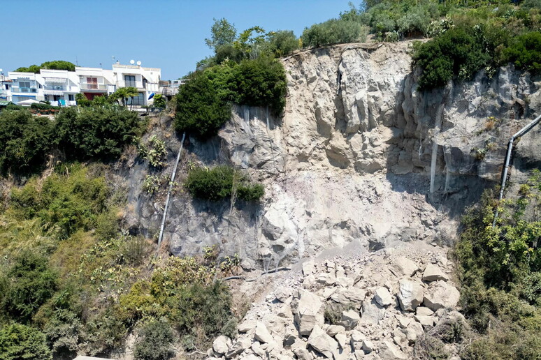 L'immagine rappresenta i Campi Flegrei, con accertamenti della Procura sulla messa in sicurezza dei costoni. Si osserva un costone roccioso con alberi e case. Il paesaggio include elementi naturali come piante e rocce, e presenta anche un edificio. Il contesto &egrave; all'aperto e caratterizzato da un ambiente naturale, con un rischio di frana evidenziato.