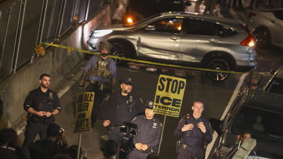 A New York, si verificano scontri dopo che l'ICE spara a un uomo. Sono presenti agenti di polizia in strada. Un'auto con un'ammaccatura si trova nella scena. Un uomo in uniforme nera tiene una macchina fotografica. La situazione &egrave; identificata come una scena del crimine.