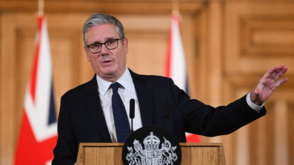 Keir Starmer, il Primo Ministro britannico, tiene una conferenza stampa riguardo al divieto dei social media per i teenager. &Egrave; riconoscibile nella foto mentre sta in piedi a un podio, con una mano alzata. Indossa un abito formale con cravatta. Attorno a lui ci sono persone che compongono il pubblico, creando un'atmosfera di discussione ufficiale.