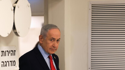 Nell'immagine, il Primo Ministro israeliano Benjamin Netanyahu &egrave; presente, indossando un abito formale con cravatta. Si osservano anche altre persone, suggerendo un contesto di celebrazione o vittoria, con riferimenti agli Stati Uniti e all'Iran. Un primo piano di una finestra &egrave; visibile, ma non &egrave; chiaro il suo significato nel contesto. La scena si svolge in un ambiente interno, probabilmente durante un evento ufficiale.