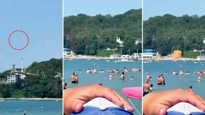 Un drone ucraino si trova sulla spiaggia, vicino al cosiddetto 'Palazzo di Putin'. La scena mostra una spiaggia affollata di persone in acqua, con un edificio bianco visibile in lontananza. L'ambiente &egrave; caratterizzato da attivit&agrave; ricreative all'aperto, come sport acquatici e nuoto, in un contesto estivo. La presenza di un frisbee suggerisce ulteriori attivit&agrave; di svago.